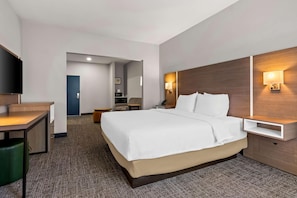 A hotel room with a bed, a desk, a chair, a TV, and a nightstand with a lamp. - Spark by Hilton Catoosa Tulsa (Catoosa)