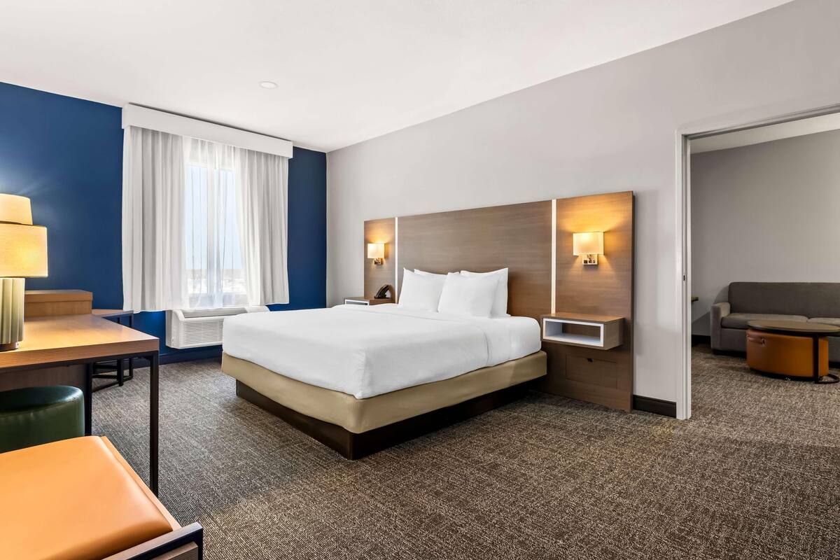 Una habitación de hotel con cama, escritorio, silla, sofá y lámpara.