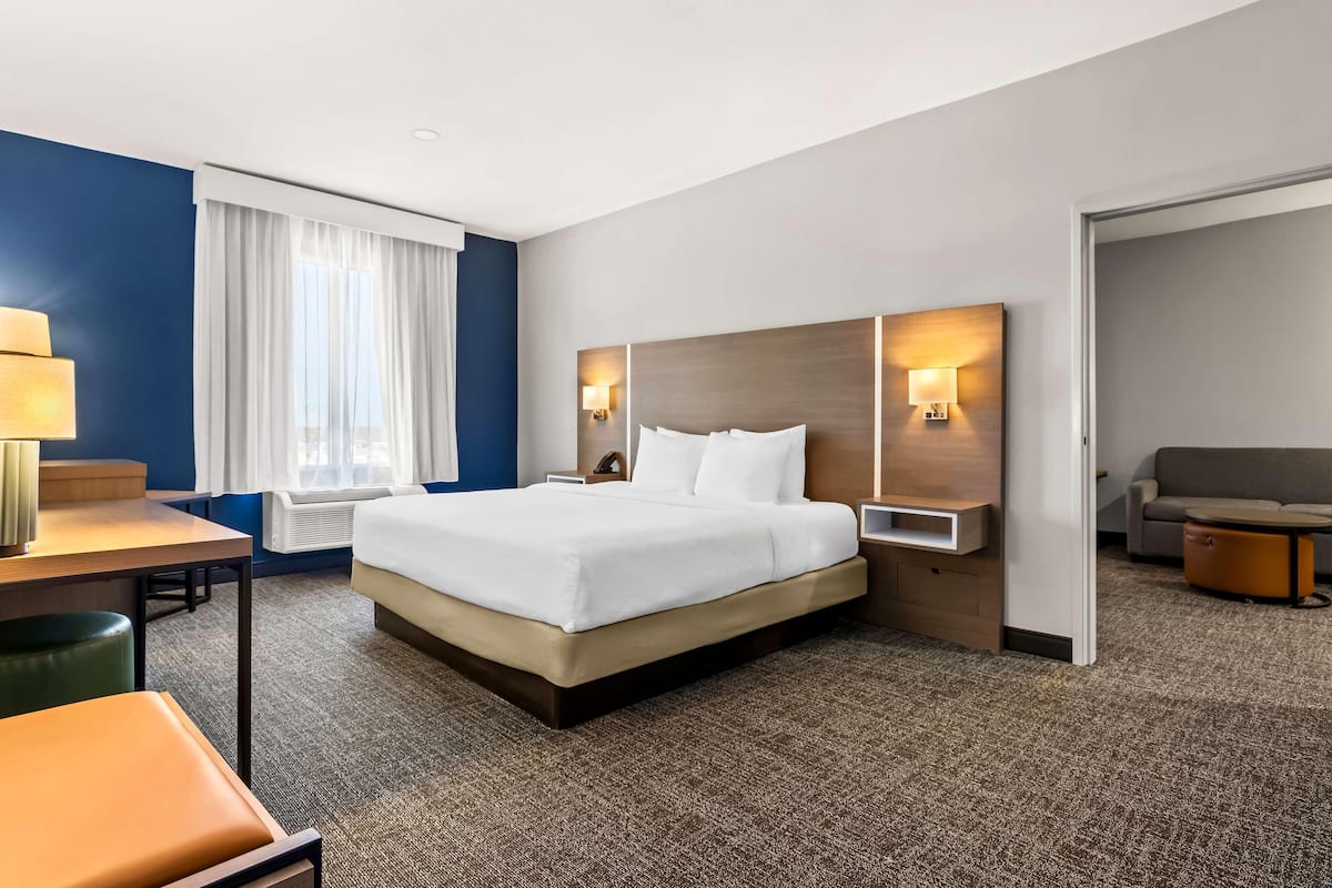 Une chambre d’hôtel avec un lit, un bureau, une chaise, un canapé et une lampe.