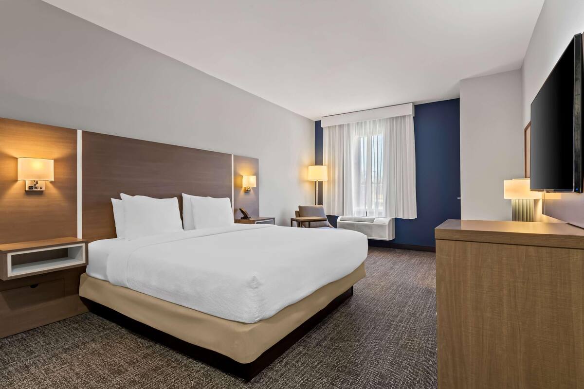 Una habitación de hotel con una cama grande, mesitas de noche, un televisor y una ventana con cortinas.