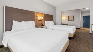 Habitación de hotel con dos camas, cabecero, lámparas de noche, escritorio y una puerta.
