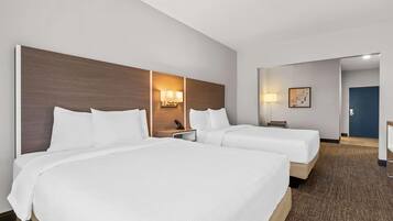 A hotel room with two beds, a headboard, bedside lamps, a desk, and a door.