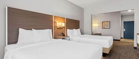 A hotel room with two beds, a headboard, bedside lamps, a desk, and a door.