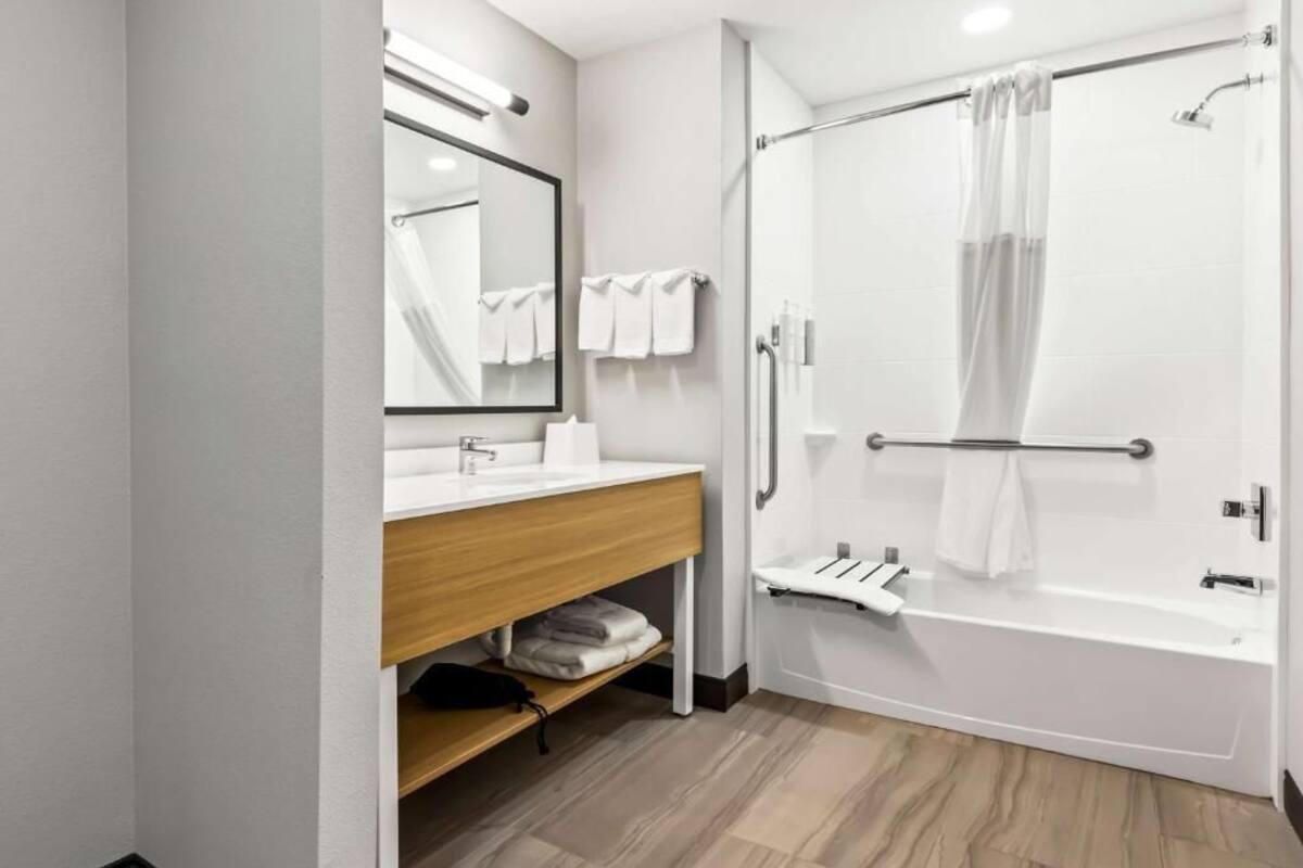 Un baño moderno con una bañera blanca, un tocador de madera, un espejo y una mampara de vidrio.