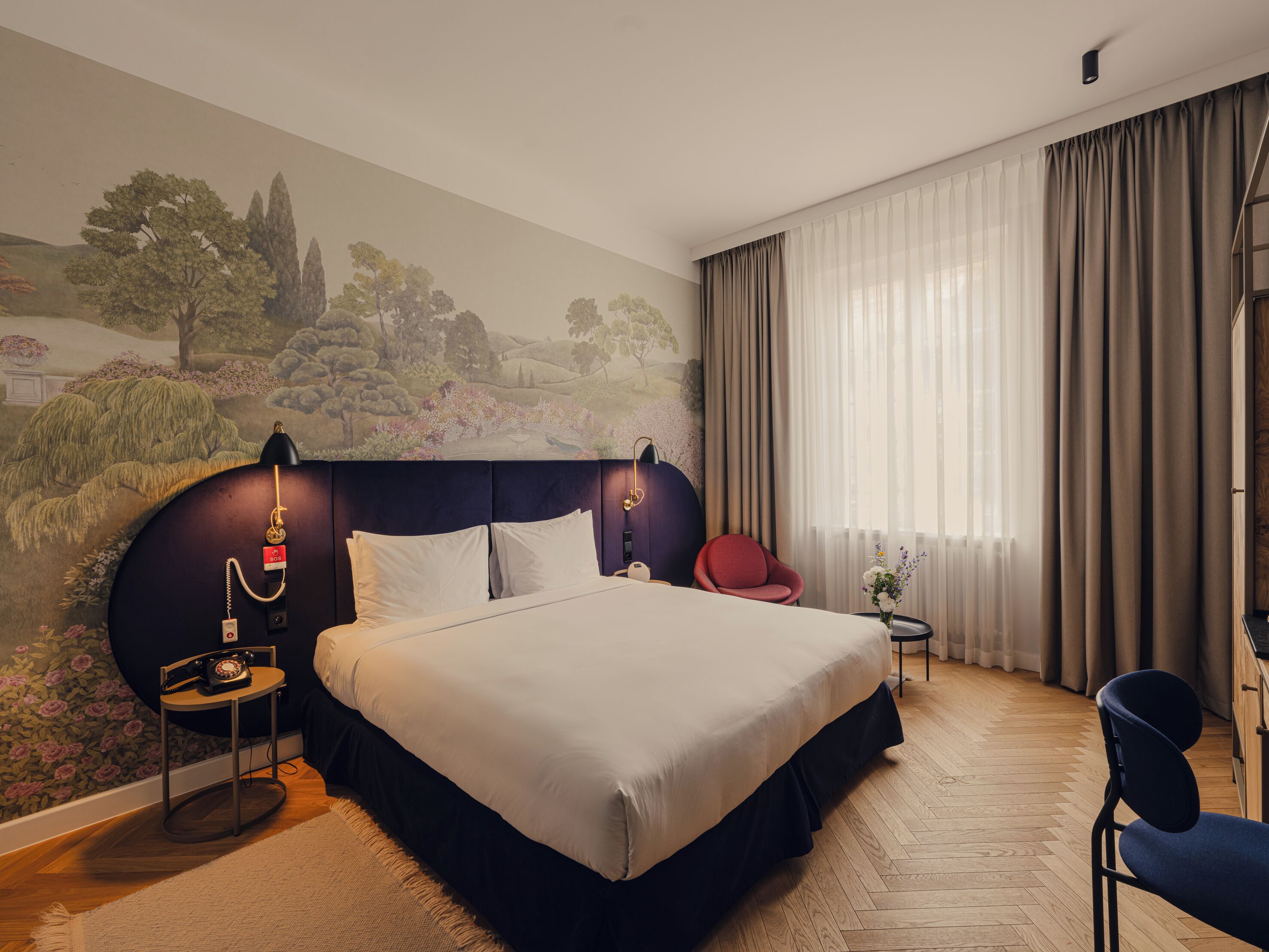 Habitación de hotel con una cama grande, una silla roja, una mesita con teléfono y un mural en la pared.