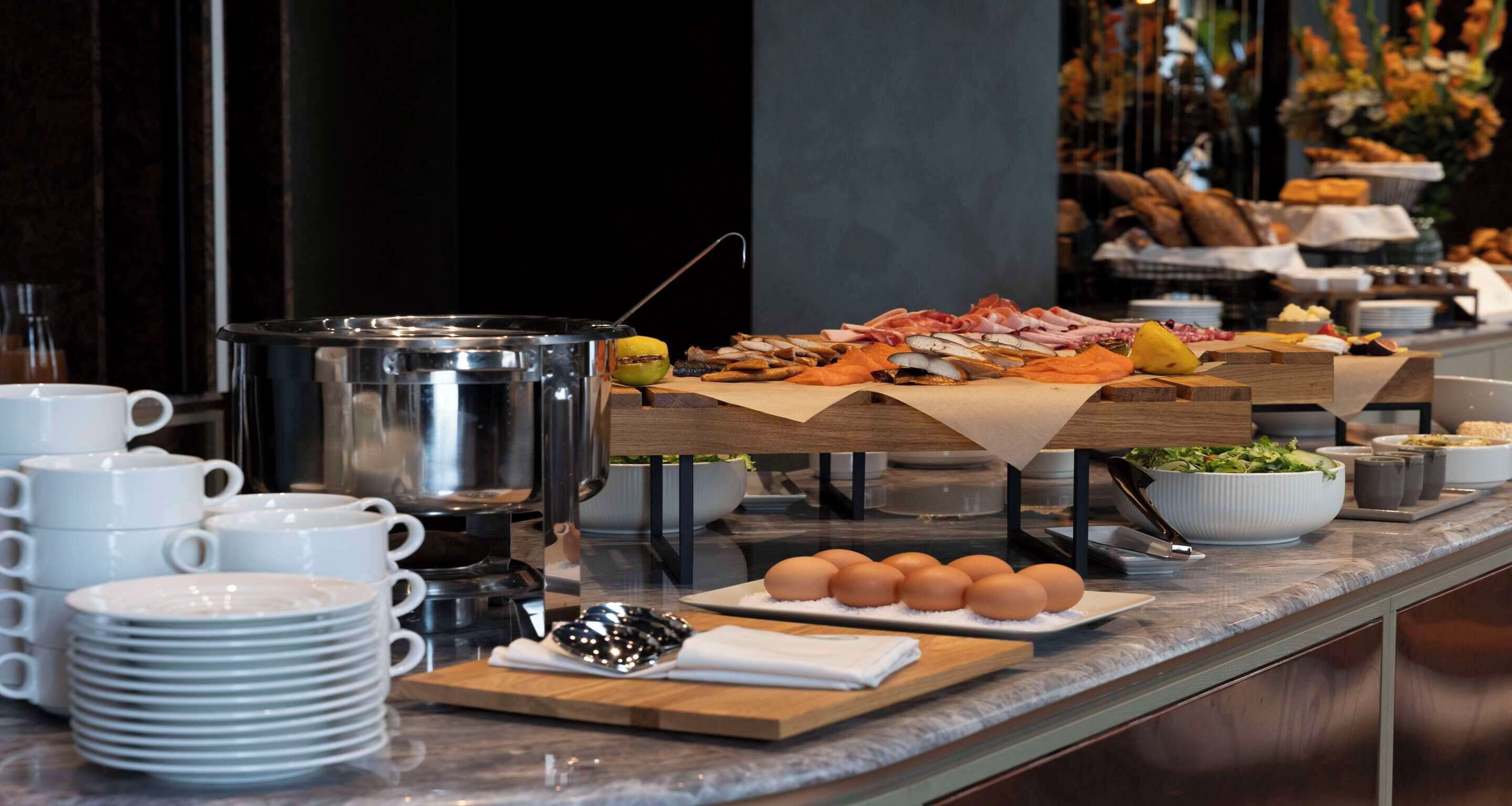 A buffet setup with various food items, including eggs, meats, and bread, on a marble countertop.