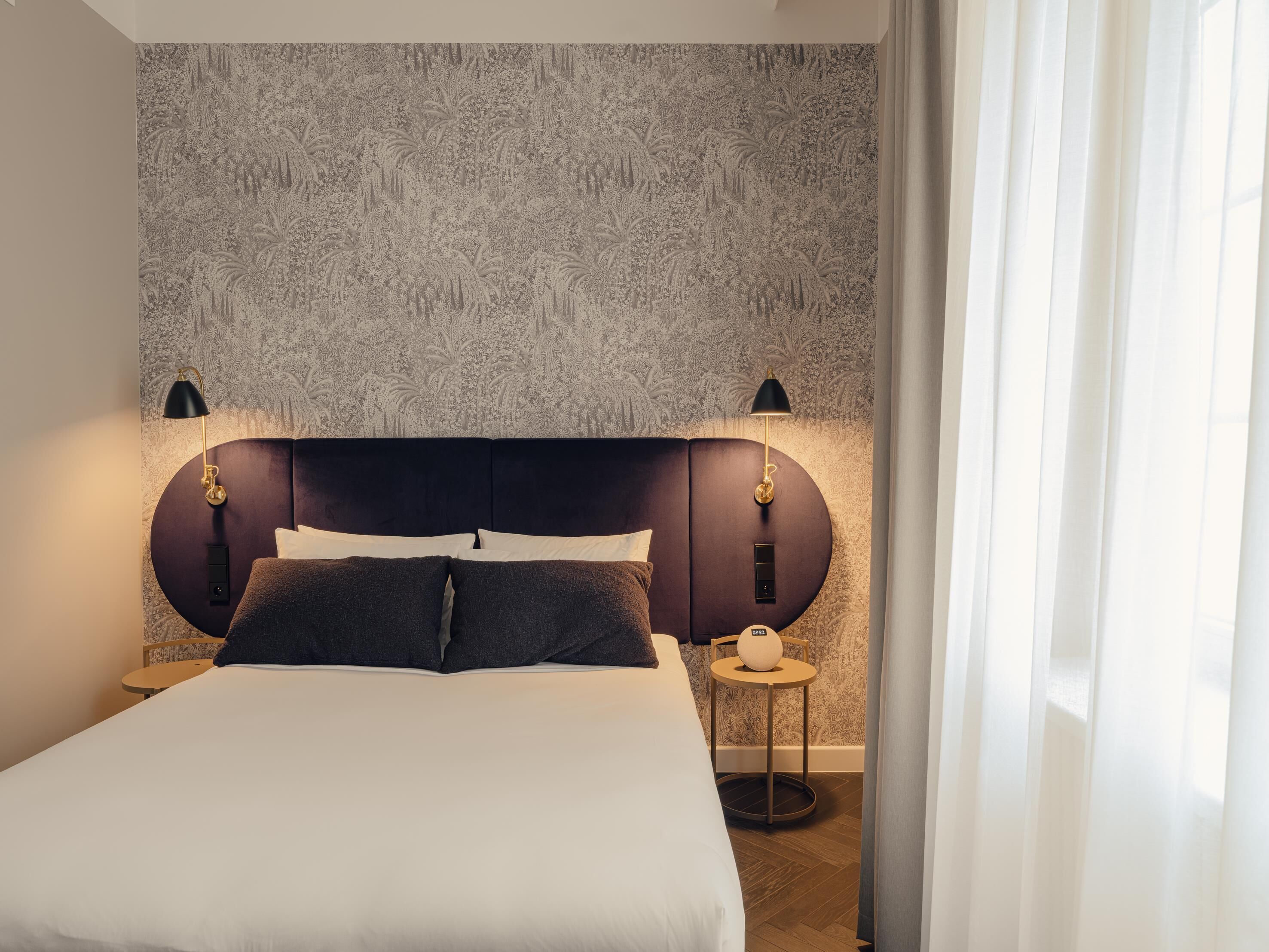 A neatly made bed with a dark headboard, two bedside lamps, and a small bedside table with a lamp.