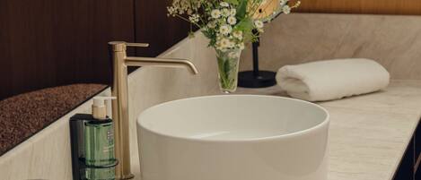 A modern bathroom with a round sink, a gold faucet, a vase of flowers, and a towel on the counter.