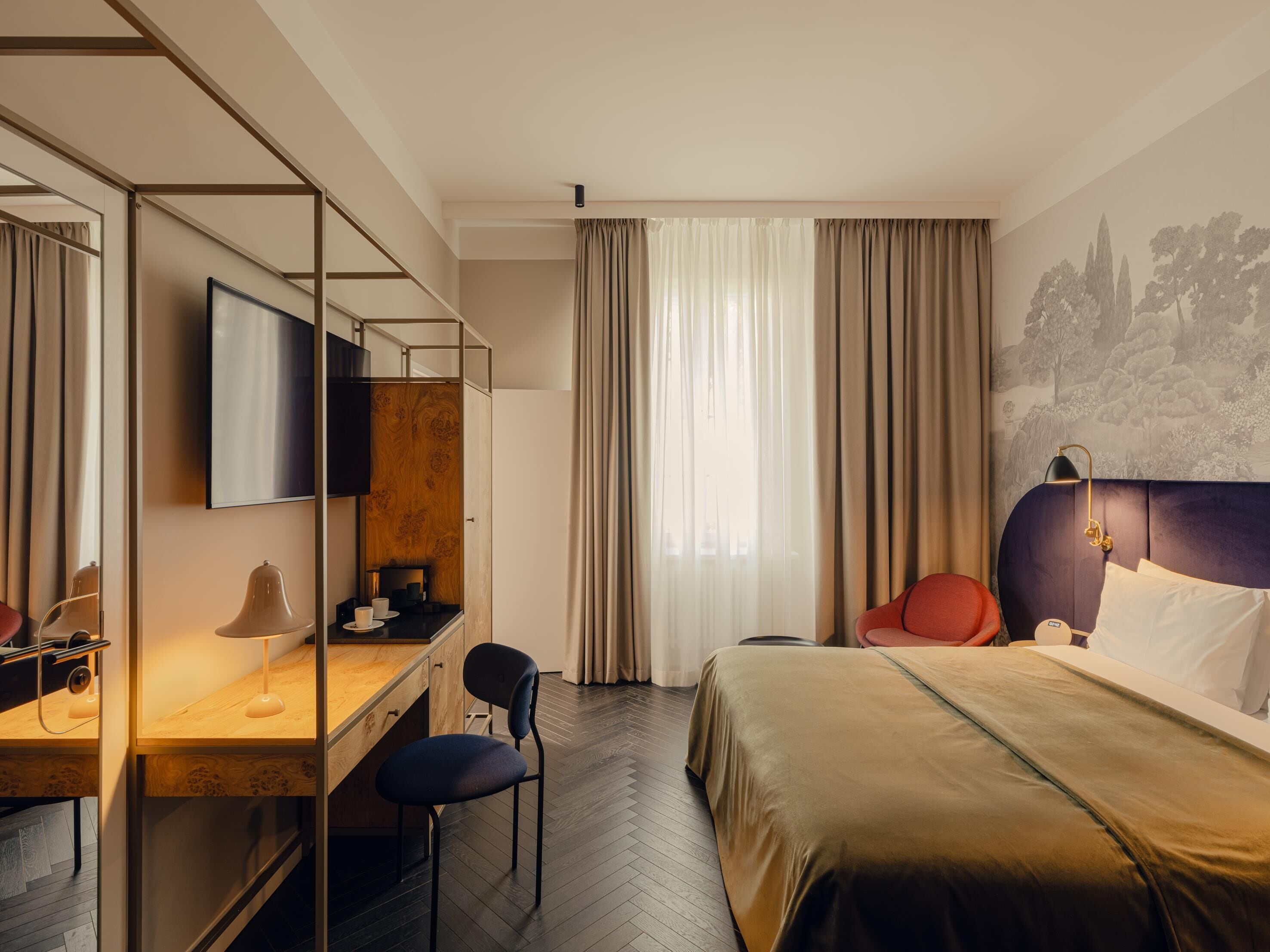 A hotel room with a bed, a desk with a chair, a TV, and a window with curtains.