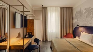 A hotel room with a bed, a desk with a chair, a TV, and a window with curtains.