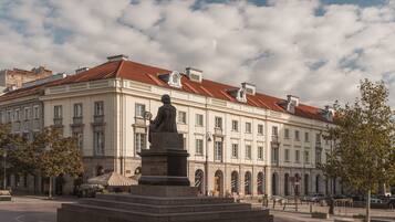 A classical building with a statue in front, featuring a central courtyard and arched windows.