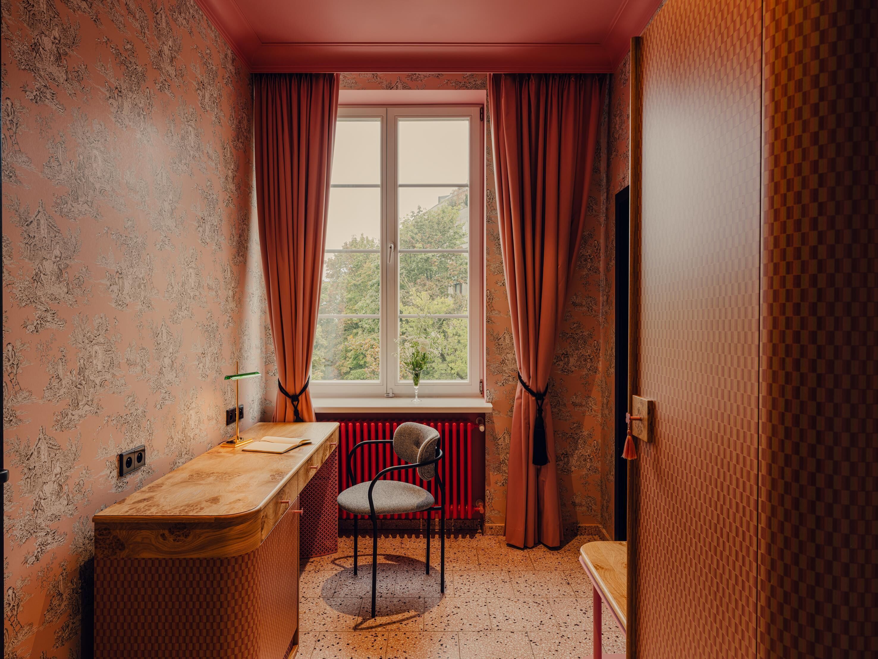 A room with a desk, chair, radiator, and a window with curtains.