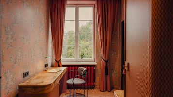 A room with a desk, chair, radiator, and a window with curtains.