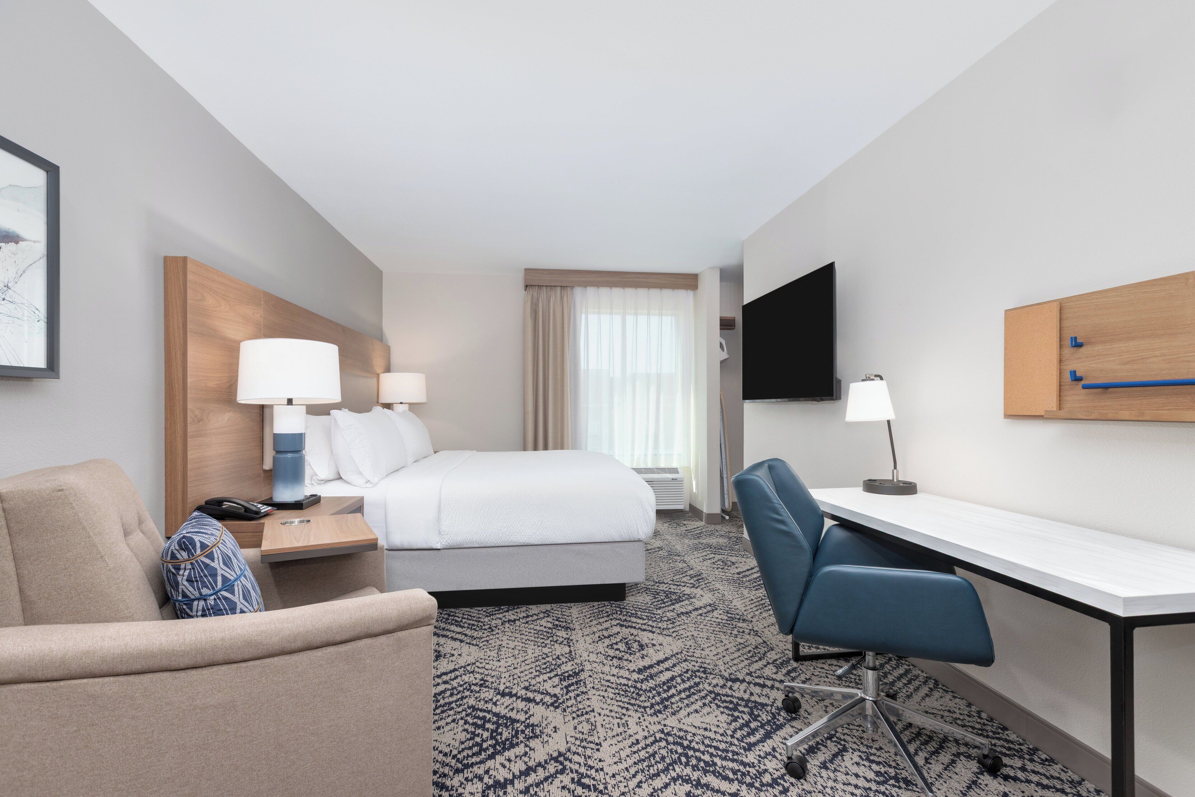 A hotel room with a bed, a desk, a chair, a TV, and a window with curtains.