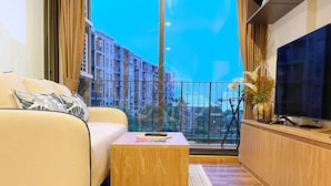 Ein modernes Wohnzimmer mit einer Couch, einem Holztisch, einem Fernseher und Blick auf Gebäude vom Balkon aus.