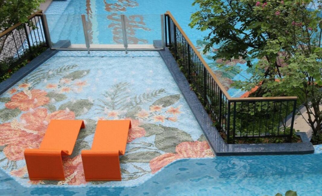 Ein Poolbereich mit floralem Dekor, zwei orangefarbene Liegestühle und ein Metallgeländer.
