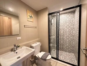 Une salle de bain avec un lavabo blanc, des toilettes et une cabine de douche dotée de portes en verre à motifs.