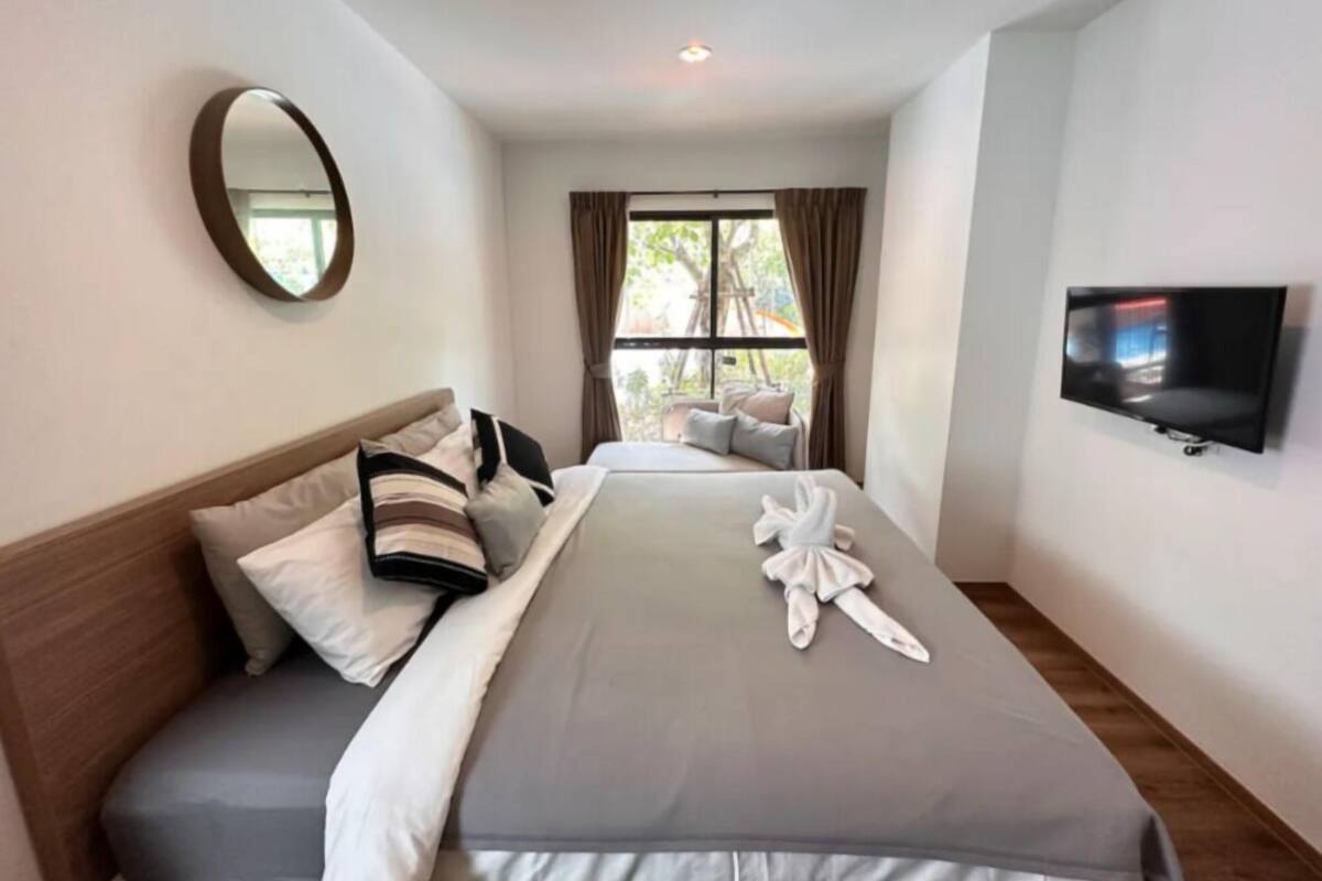 Una habitación de hotel con una cama, televisor, ventana con cortinas y un espejo en la pared.