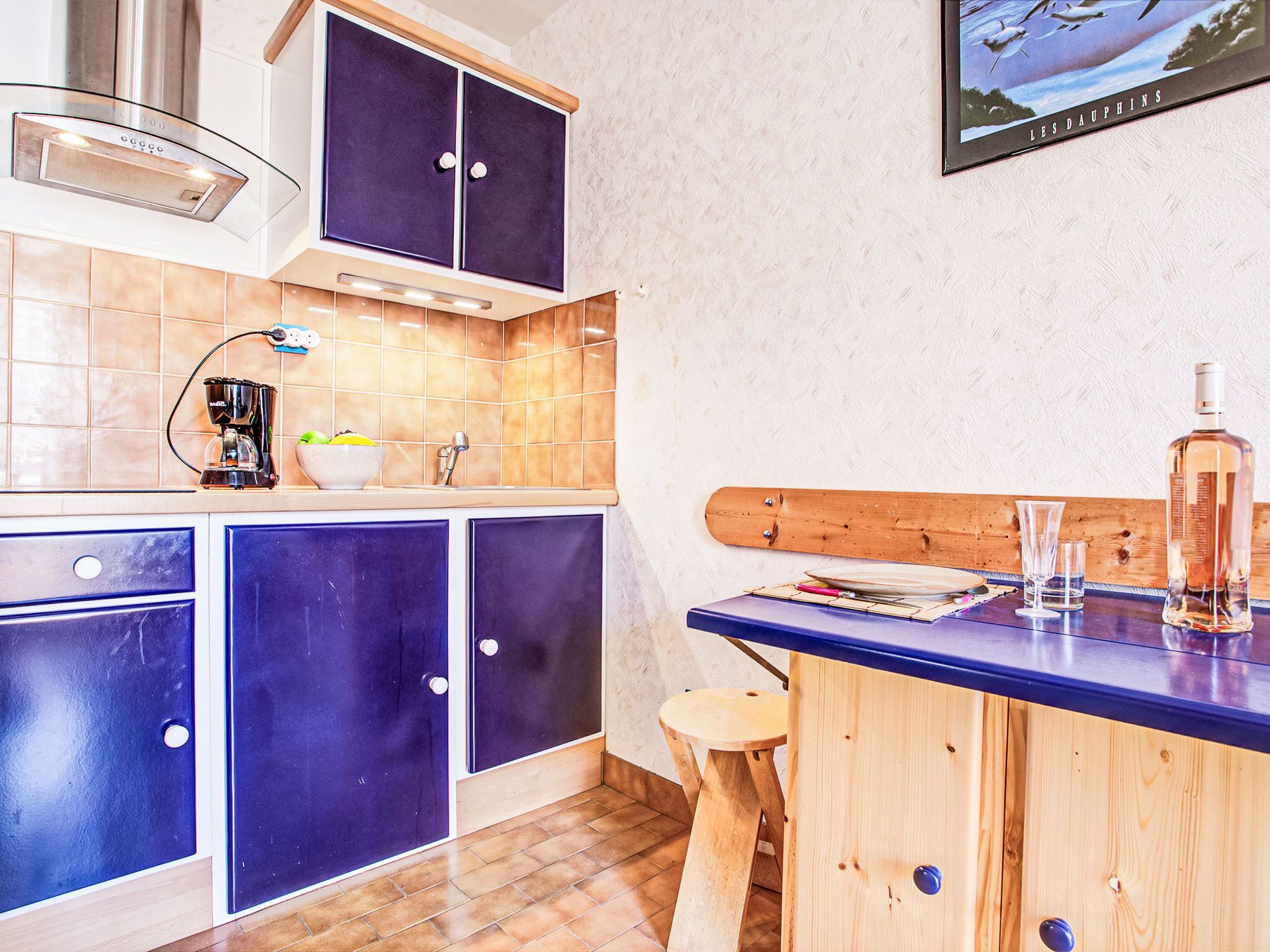 A kitchen with blue cabinets, a coffee maker, and a wooden bar counter with glasses and a bottle.