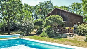 Una cabaña de madera con piscina, rodeada de árboles y follaje.