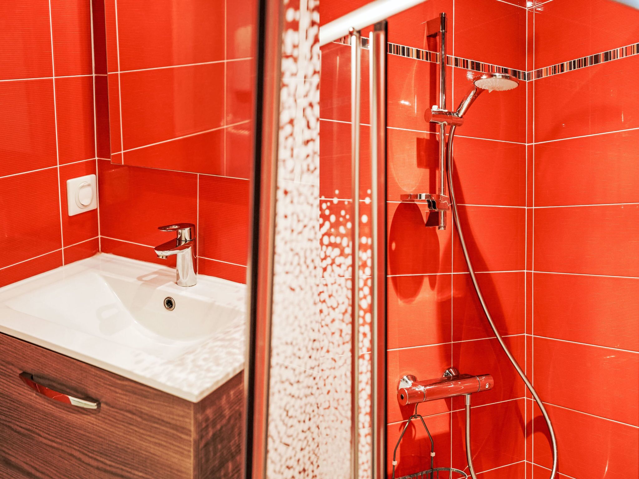 A bathroom with a white sink, red tiled walls, and a glass shower enclosure.