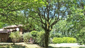 Un patio arbolado con un edificio de ladrillo, un pequeño pabellón y una zona verde.