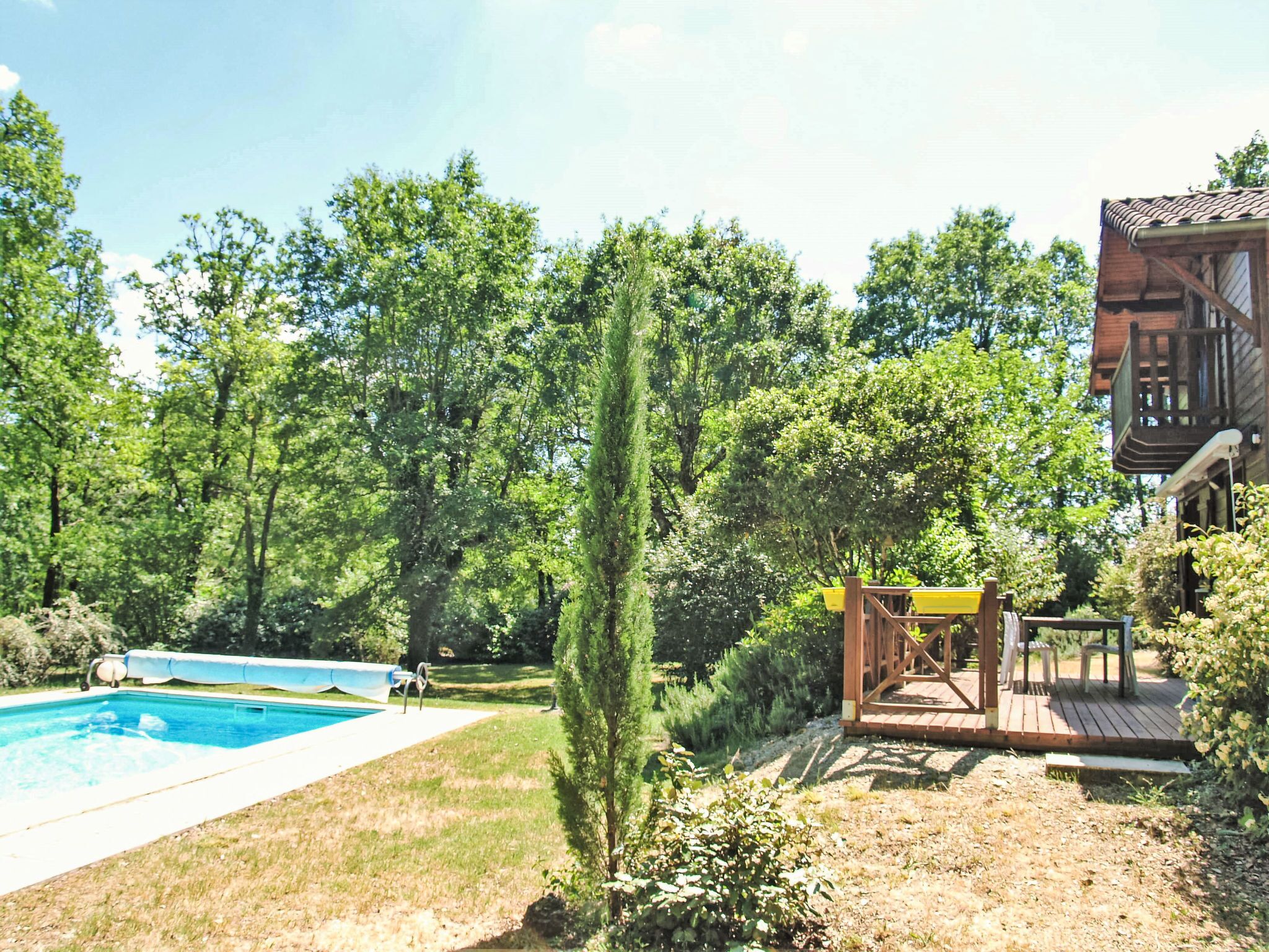 A backyard with a swimming pool, wooden deck, and a wooden cabin.