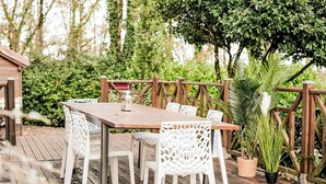 Una terraza de madera al aire libre con una mesa y sillas, rodeada de follaje y una valla de madera.