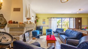 A cozy living room with a fireplace, leather sofas, a dining table set for four, and a large window offering a view of the outdoors. - La mouette bleue by Interhome (Loctudy)