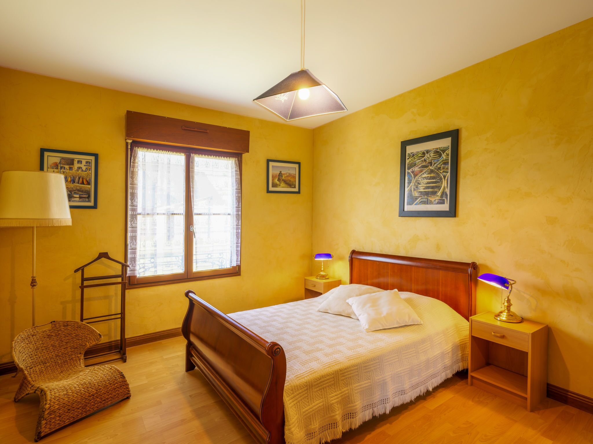A bedroom with a wooden bed, a hanging chair, a window with curtains, and two bedside lamps.