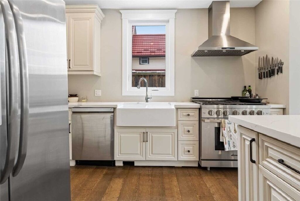 Una cocina moderna con armarios blancos, electrodomésticos de acero inoxidable y un ventanal sobre el fregadero.