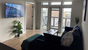 A modern living room with a large TV, a ceiling fan, and a balcony with a view of buildings. - Deep Ellum Lux apartment with endless amenities! (Dallas)