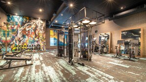 A gym with various exercise equipment, a graffiti-covered wall, and a brick wall with ventilation ducts. - Deep Ellum Lux apartment with endless amenities! (Dallas)