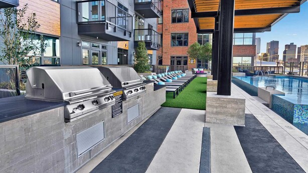 An outdoor barbecue area with a grill, seating, and a pool. - Deep Ellum Lux apartment with endless amenities! (Dallas)