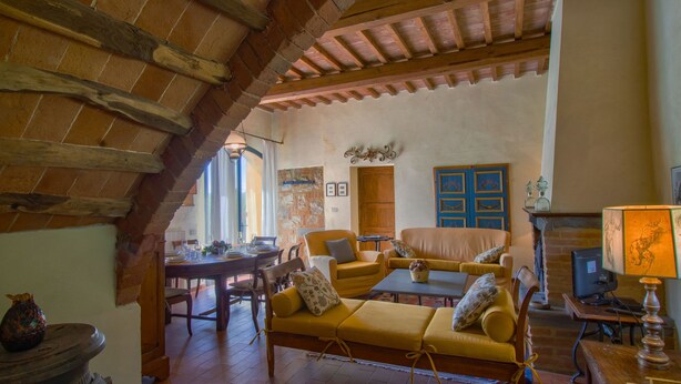 A rustic interior with exposed wooden beams, a stone fireplace, and a dining area with a table set for two.