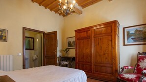A bedroom with a bed, wooden wardrobe, a chair, and a painting on the wall.