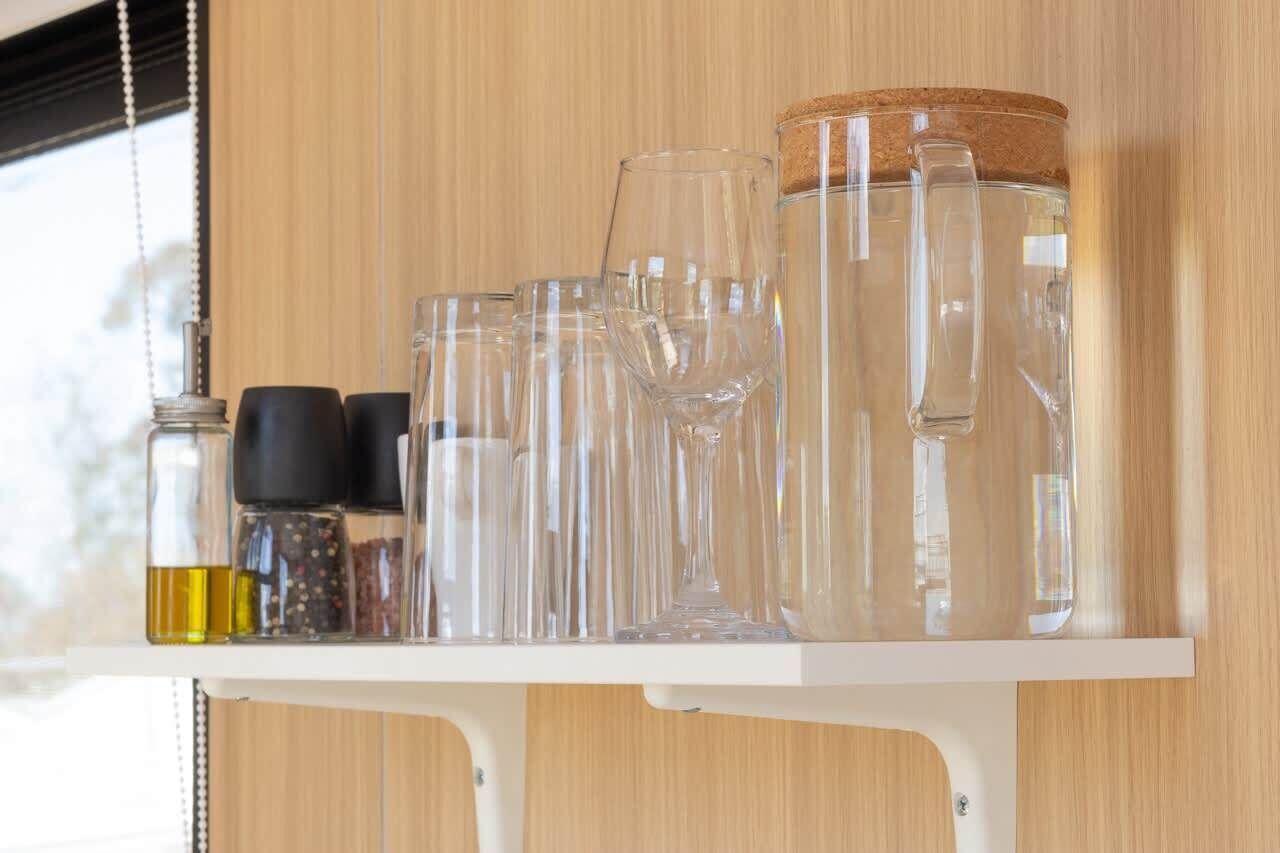 A shelf with various glass containers and a jar of water.