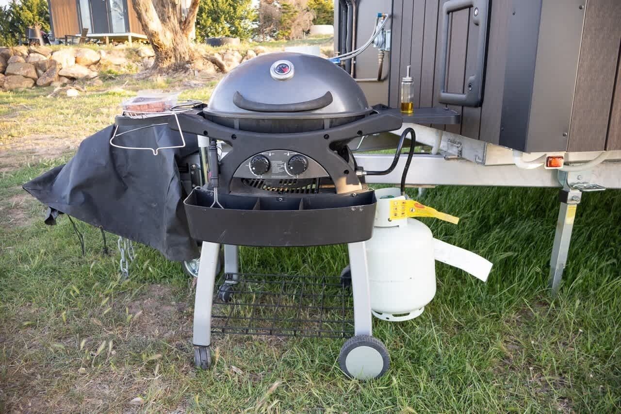 Una parrilla portátil con funda negra, un tanque de gas y un soporte de metal.