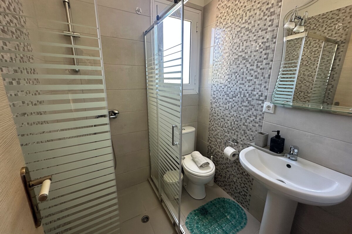 Un baño con cabina de ducha de vidrio, inodoro, lavamanos y espejo.
