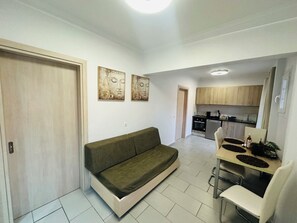 A modern living room with a sofa, a dining table with chairs, and a kitchen area in the background. - Nikos Apartments Corfu (Corfu)