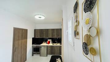 Une cuisine moderne avec des meubles en bois foncé, un four encastré et un réfrigérateur. On y trouve un coin repas avec une table et des chaises noires, ainsi qu’un élément décoratif mural orné de motifs circulaires et floraux.