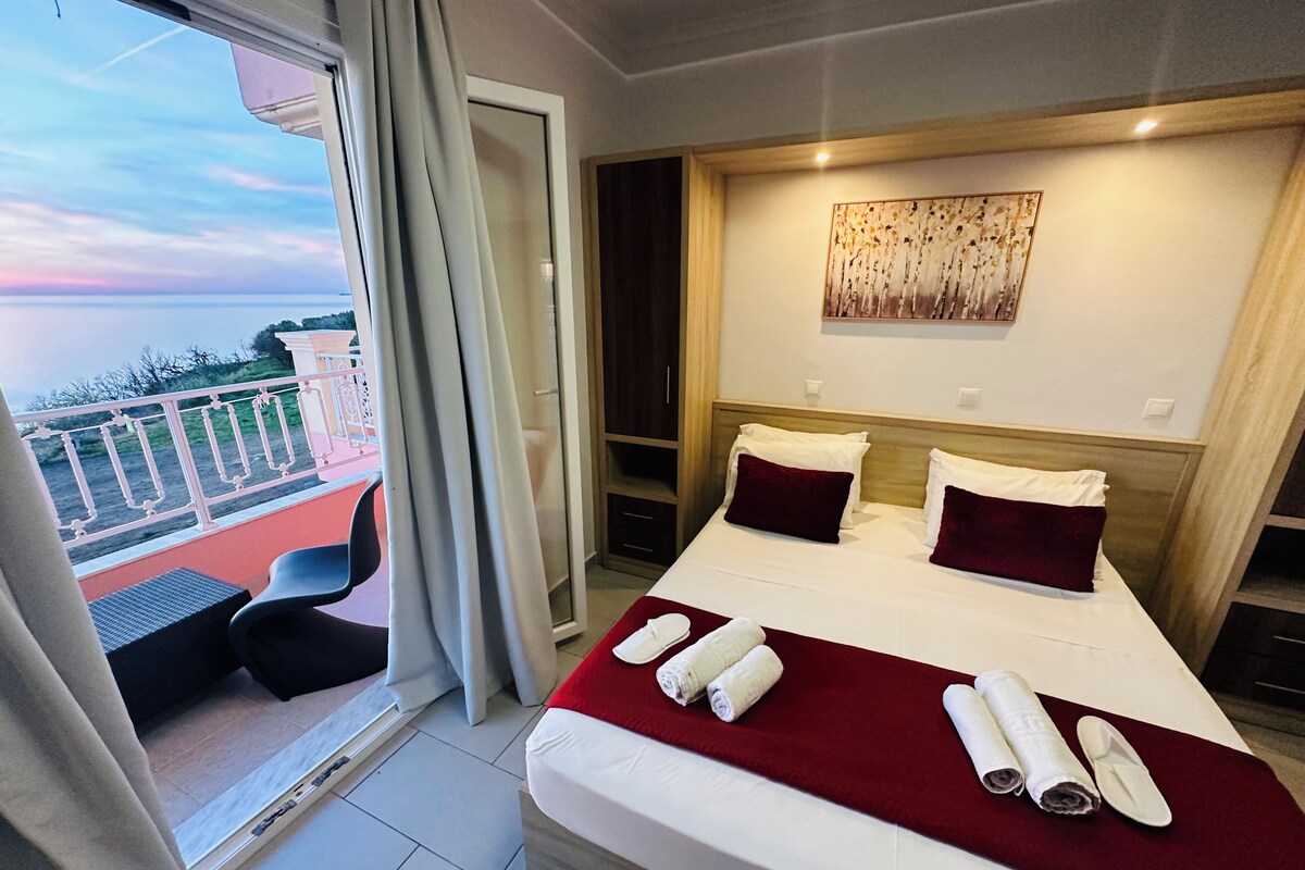 A hotel room with a large bed, a balcony with a view, and a painting on the wall.