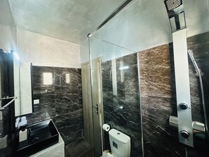 Un baño moderno con cabina de ducha de vidrio, pared con azulejos de mármol y lavamanos con encimera negra.