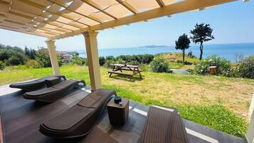 Un espacio al aire libre cubierto con sillones reclinables, una mesa de picnic y vistas al mar.