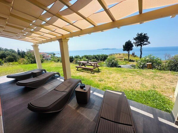 Un espacio al aire libre cubierto con sillones reclinables, una mesa de picnic y vistas al mar.