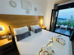A hotel room with a large bed, two bedside lamps, a wooden headboard, and a view of a balcony with outdoor furniture. - Nikos Apartments Corfu (Corfu)