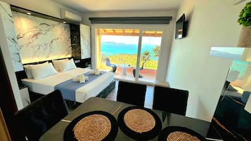 Quarto de hotel moderno com cama, área de jantar e varanda com vista.