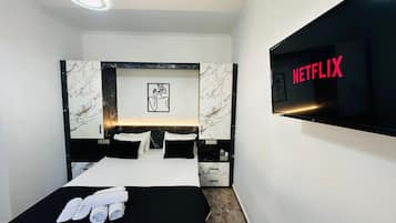 Quarto de hotel moderno com uma cama grande, uma TV de tela plana exibindo o logotipo da Netflix, cabeceira com padrão de mármore e uma obra de arte emoldurada acima da cama.