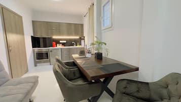 Une cuisine moderne avec des meubles de couleur sombre, un four encastré et un coin repas comprenant une table en bois et deux chaises grises recouvertes de tissu.