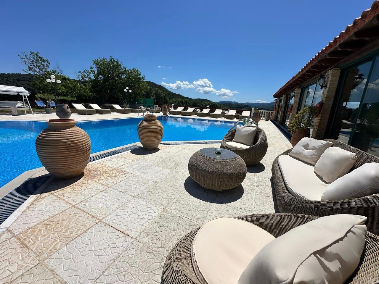 A poolside area with wicker furniture, large vases, and a clear view of the surrounding landscape.